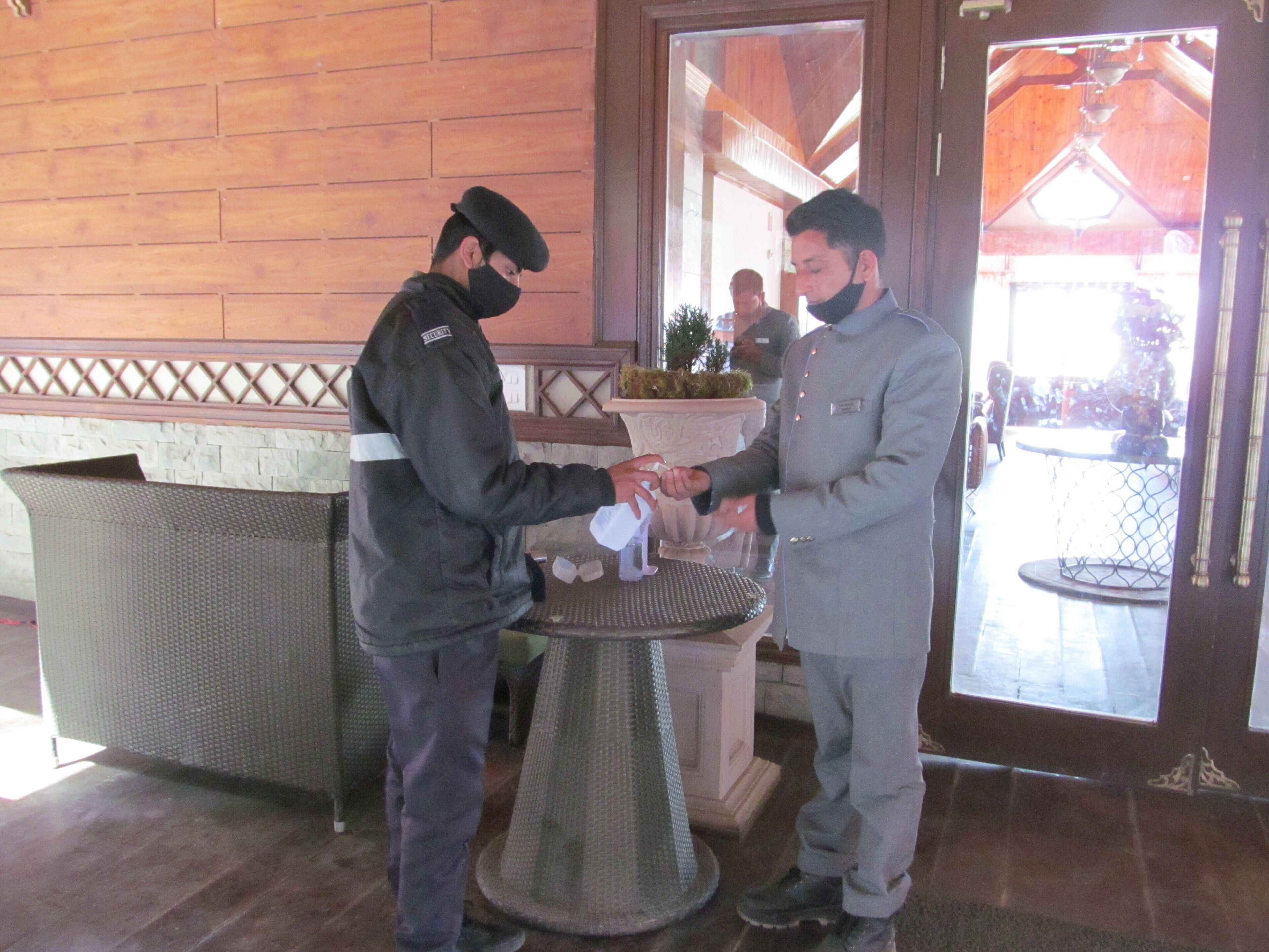 Two men in uniform handing over a white object to each other in a lobby with wooden walls and a glass door.