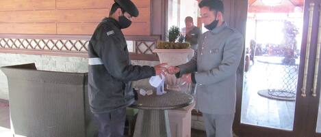 Two men in uniform handing over a white object to each other in a lobby with wooden walls and a glass door.