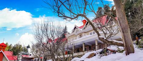 A snow-covered building with a red roof, stone walls, and a staircase leading up to the entrance.