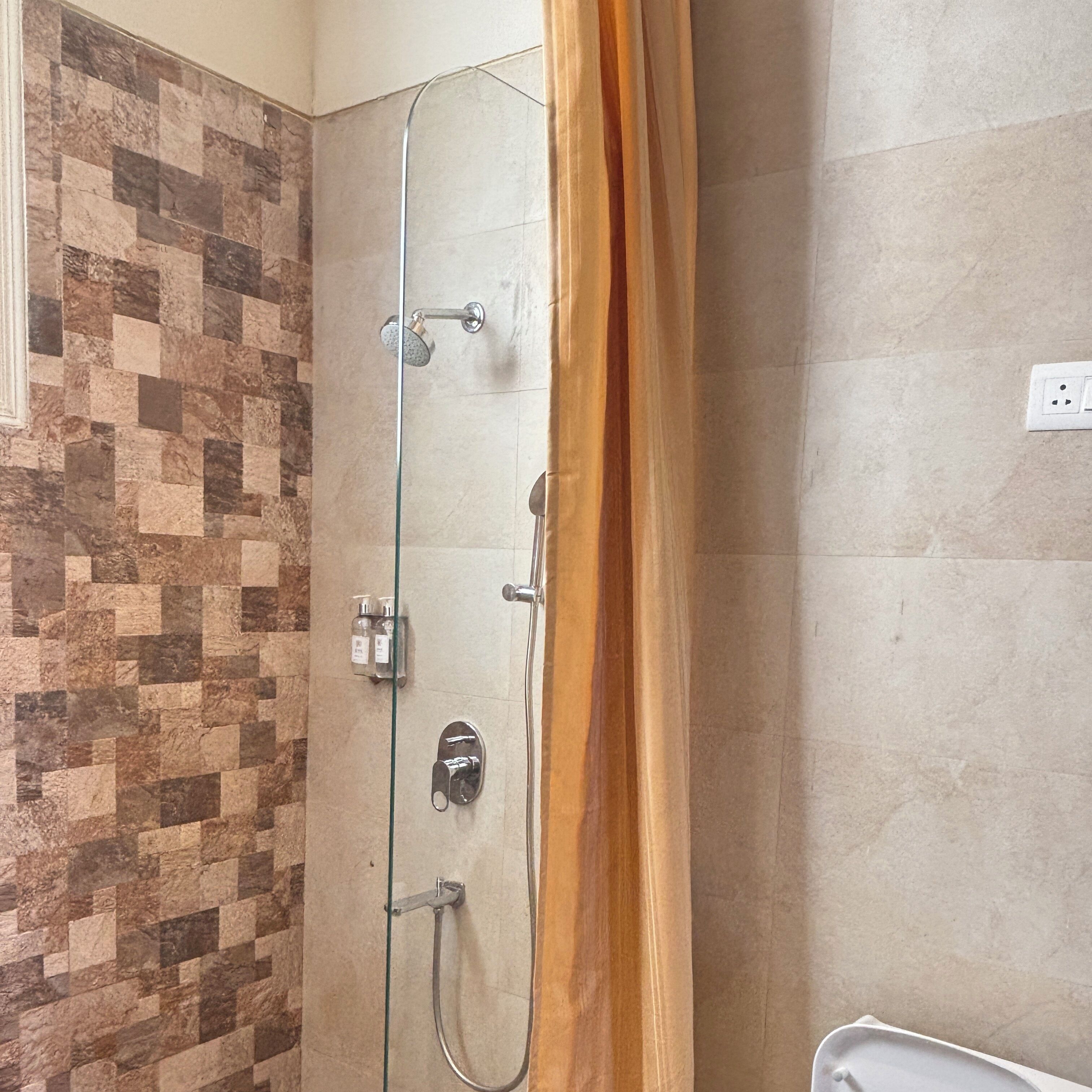 A shower with a glass door, a tiled wall with a geometric pattern, and a plain wall with a power outlet.