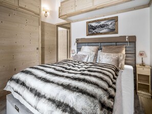A bedroom with a large bed, wooden walls, a mounted picture, and a bedside table with a lamp.