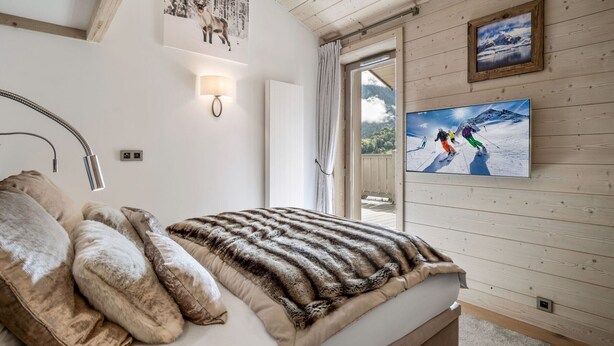 Une chambre à coucher avec un lit, un téléviseur fixé au mur et une fenêtre avec des rideaux.