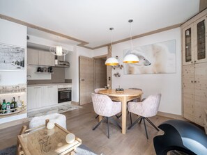 A modern kitchen with wooden cabinets, a dining area with a round table and chairs, and a large painting on the wall.