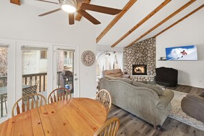 Ein Wohnzimmer mit Kamin aus Stein, einem an der Wand befestigten Fernseher und einem Essbereich mit Holztisch und Stühlen.