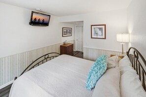 Un dormitorio con una cama, televisor montado en la pared, una puerta y una lámpara.