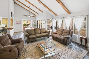 A spacious living room with a sofa set, a glass coffee table, and a view of the outdoors. - Ski and Tee by Destination Big Bear : Choice Bear Meadows Townhome! PET FRIENDLY 🐾! Walk to Bear Mountain Resort and Golf Course! (Big Bear Lake)