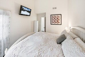 A bedroom with a bed, a television, a framed picture, and a door. - Ski and Tee by Destination Big Bear : Choice Bear Meadows Townhome! PET FRIENDLY 🐾! Walk to Bear Mountain Resort and Golf Course! (Big Bear Lake)