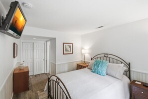 Ein Schlafzimmer mit einem Bett, Nachttischen, einem an der Wand montierten Fernseher, einer Tür und einem gerahmten Bild.