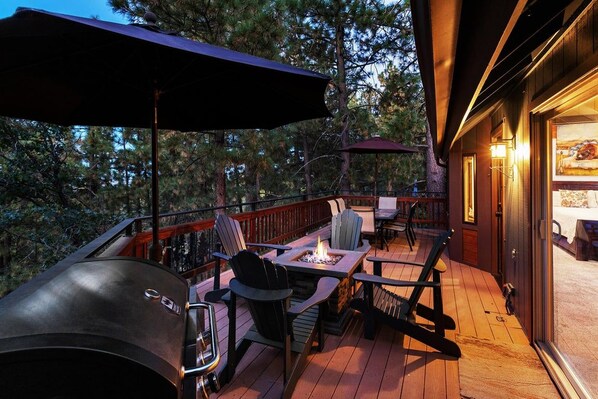 An outdoor deck with a grill, seating area, and a view of the forest.