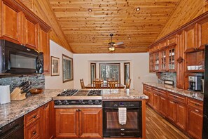 A kitchen with wooden cabinets, granite countertops, a gas stove, and a dishwasher. - Relax and Enjoy the Peace and Quiet in Luxury! Upper Moonridge! Hot Tub! Pet Friendly! Gameroom! Peloton Bike! (Big Bear City)