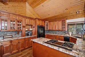 Une cuisine avec des meubles en bois, des plans de travail en granit, un réfrigérateur noir et une cuisinière à gaz.
