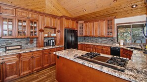 Eine geräumige Küche mit Holzausstattung, einer Granitarbeitsplatte, einem schwarzen Kühlschrank und einem eingebauten Gasherd.
