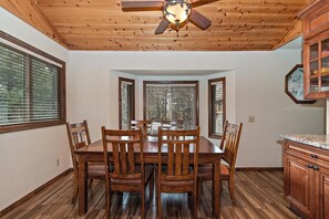 A dining area with a wooden table and chairs, a ceiling fan, and windows with blinds. - Relax and Enjoy the Peace and Quiet in Luxury! Upper Moonridge! Hot Tub! Pet Friendly! Gameroom! Peloton Bike! (Big Bear City)
