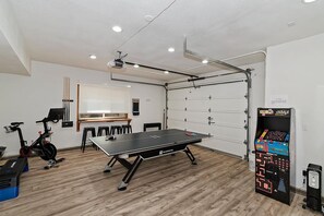 A room with a ping pong table, exercise bike, and a gaming machine. - Relax and Enjoy the Peace and Quiet in Luxury! Upper Moonridge! Hot Tub! Pet Friendly! Gameroom! Peloton Bike! (Big Bear City)