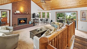 A spacious living room with a fireplace, a ceiling fan, and a view of the outdoors. - Relax and Enjoy the Peace and Quiet in Luxury! Upper Moonridge! Hot Tub! Pet Friendly! Gameroom! Peloton Bike! (Big Bear City)