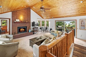 A spacious living area with a fireplace, a ceiling fan, and a view of the outdoors.
