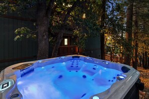 A hot tub in a wooded area with a wooden deck and a building in the background. - Relax and Enjoy the Peace and Quiet in Luxury! Upper Moonridge! Hot Tub! Pet Friendly! Gameroom! Peloton Bike! (Big Bear City)