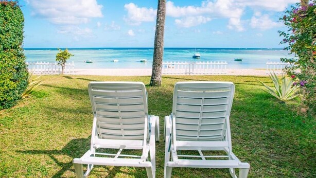 Twee witte lounge stoelen gericht op een strand met helderblauw water en een witte omheining op de achtergrond.
