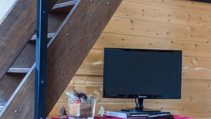 Interior de uma cabana de madeira com uma televisão em uma cômoda de madeira, um copo de água e um tecido vermelho.