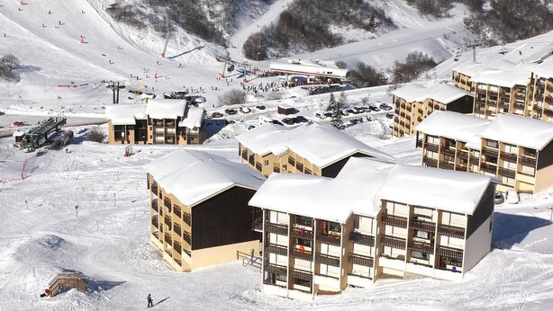 Uma estância de esqui com vários edifícios em estilo chalé, teleféricos e uma paisagem coberta de neve.