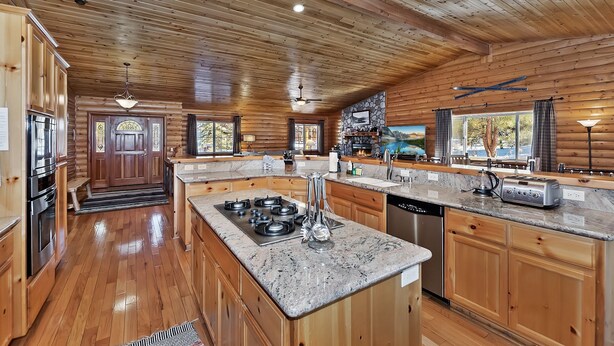 A spacious log cabin kitchen with granite countertops, stainless steel appliances, and a stone fireplace. - Stork and Bear Cabin by Destination Big Bear : Luxury Log Home in Eagle Mountain Estates! Pool Table! (Big Bear Lake)