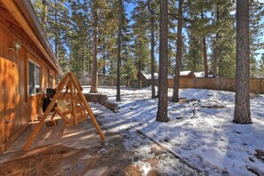 Una cabaña de madera con un columpio en un bosque nevado.