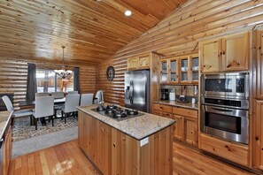 Cocina estilo cabaña con gabinetes de madera, una isla central, electrodomésticos de acero inoxidable y una zona de comedor con mesa y sillas.