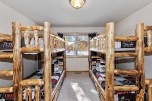 Una habitación con literas de madera, una ventana con vistas a árboles y piso alfombrado.