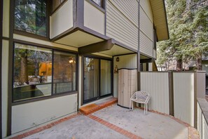 A residential building with a covered patio, a sliding glass door entrance, and a white chair outside. - Snow Summit Chalet by Destination Big Bear : Next Door to Snow Summit for Easy Access to Skiing, Snowboarding and Tubing! (Big Bear Lake)