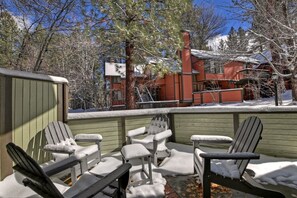 A covered outdoor seating area with Adirondack chairs, a wooden deck, and a view of a red building with a chimney.