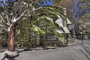 A single-story building with a snow-covered roof and a large tree in front.