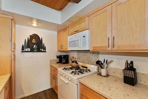 A kitchen with wooden cabinets, a gas stove, a microwave, and a coffee maker. - Snow Summit Chalet by Destination Big Bear : Next Door to Snow Summit for Easy Access to Skiing, Snowboarding and Tubing! (Big Bear Lake)