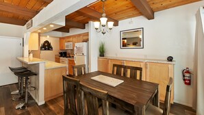A kitchen with wooden cabinets, a dining table, and bar stools. - Snow Summit Chalet by Destination Big Bear : Next Door to Snow Summit for Easy Access to Skiing, Snowboarding and Tubing! (Big Bear Lake)