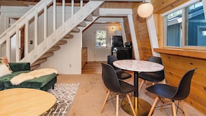 A cozy interior with a staircase, a dining area with a round table and chairs, and a view of the outdoors through a window. - Lower Moonridge! Close to Zoo, Bear Mountain Resort, Golf Course & Hiking/Biking Trails! Fenced Yard! (Big Bear Lake CA)