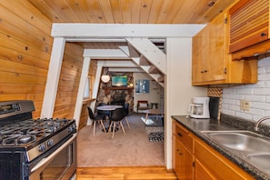 A kitchen with a gas stove, wooden cabinets, a stone fireplace, and a dining area with chairs. - Lower Moonridge! Close to Zoo, Bear Mountain Resort, Golf Course & Hiking/Biking Trails! Fenced Yard! (Big Bear Lake CA)