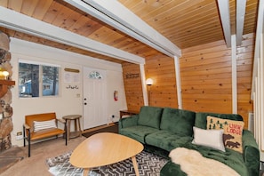 A cozy cabin interior with a green sofa, a wooden table, and a stone wall. - Lower Moonridge! Close to Zoo, Bear Mountain Resort, Golf Course & Hiking/Biking Trails! Fenced Yard! (Big Bear Lake CA)