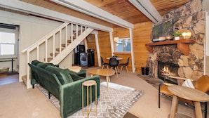 A cozy living room with a green sofa, a fireplace, a stone wall, and a staircase leading to another level. - Lower Moonridge! Close to Zoo, Bear Mountain Resort, Golf Course & Hiking/Biking Trails! Fenced Yard! (Big Bear Lake CA)