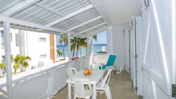 A covered outdoor seating area with a table and chairs, a view of the ocean, and a door with a security camera.