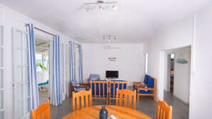 A dining area with a round wooden table, blue cushioned chairs, a television, and a ceiling fan.