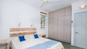 A bedroom with a bed, wooden headboard, two bedside tables, a window with a view, a wardrobe, and a door.