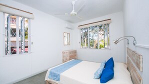 A bedroom with a bed, a ceiling fan, a window with a view, and a nightstand.