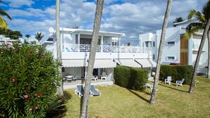 Un edificio blanco de dos pisos con un balcón, rodeado de palmeras y un césped cuidado.