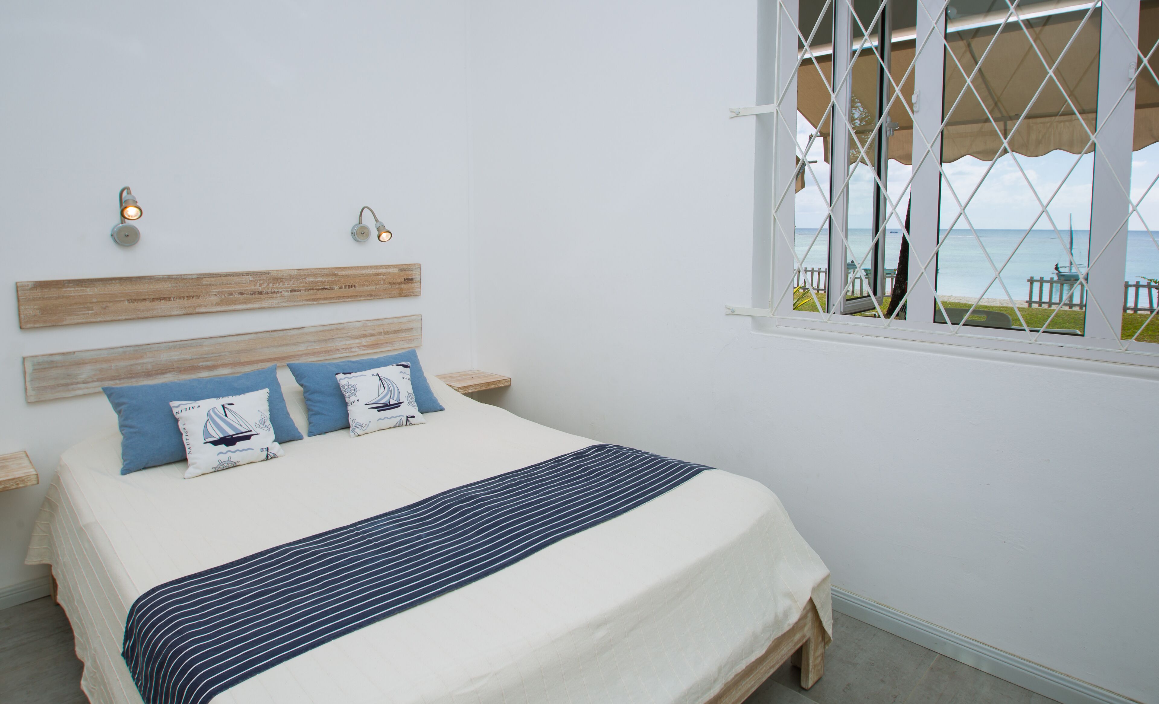 A bedroom with a bed, two bedside tables, a window with a view of the sea, and a wooden headboard.