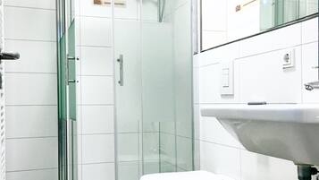 Ein modernes Badezimmer mit einer glasumschlossenen Dusche, einer weißen Toilette und einem Waschbecken mit Spiegel darüber.