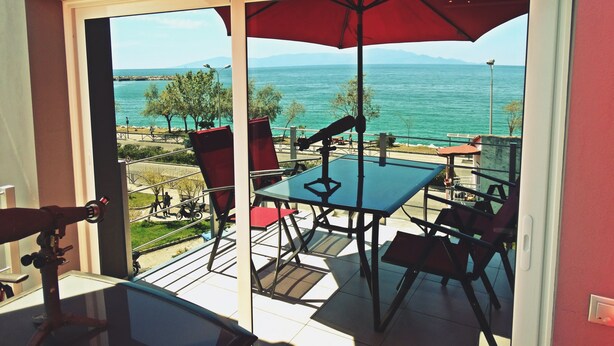 Ein Balkon mit Tisch und Stühlen, mit Blick auf eine reizvolle Landschaft aus Meer und Bergen.