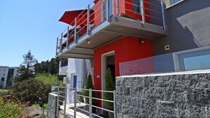 Ein modernes Gebäude mit roter und grauer Fassade, ein Balkon mit rotem Sonnenschirm und eine Steinmauer im Vordergrund.