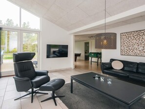 Een moderne woonkamer met een zwarte leren bank, een zwarte lederen fauteuil, een salontafel en een televisie die aan de muur is bevestigd.