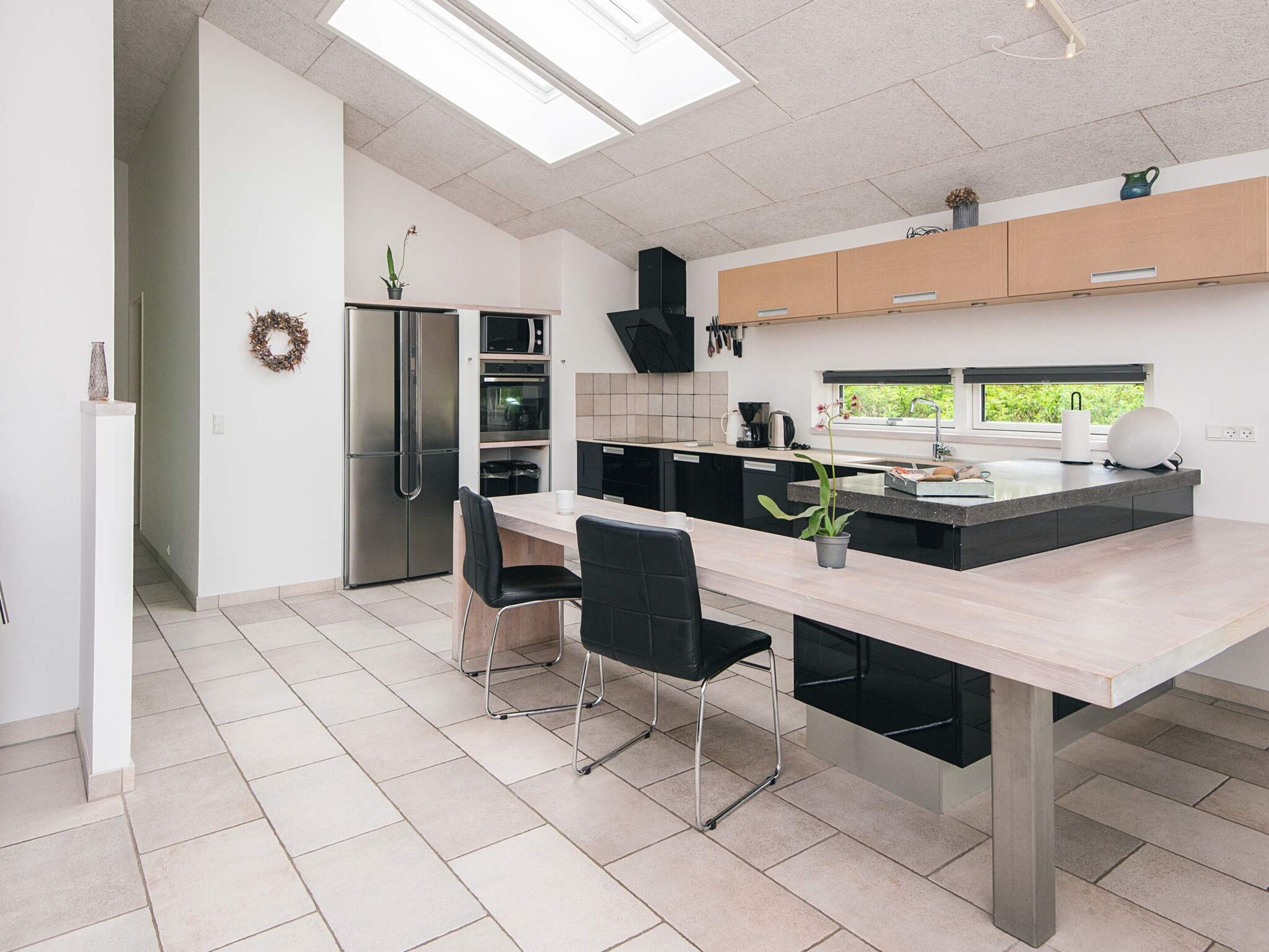 A modern kitchen with a central island, black chairs, and a stainless steel refrigerator.