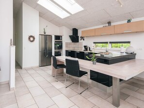 A modern kitchen with a central island, black chairs, and a stainless steel refrigerator.