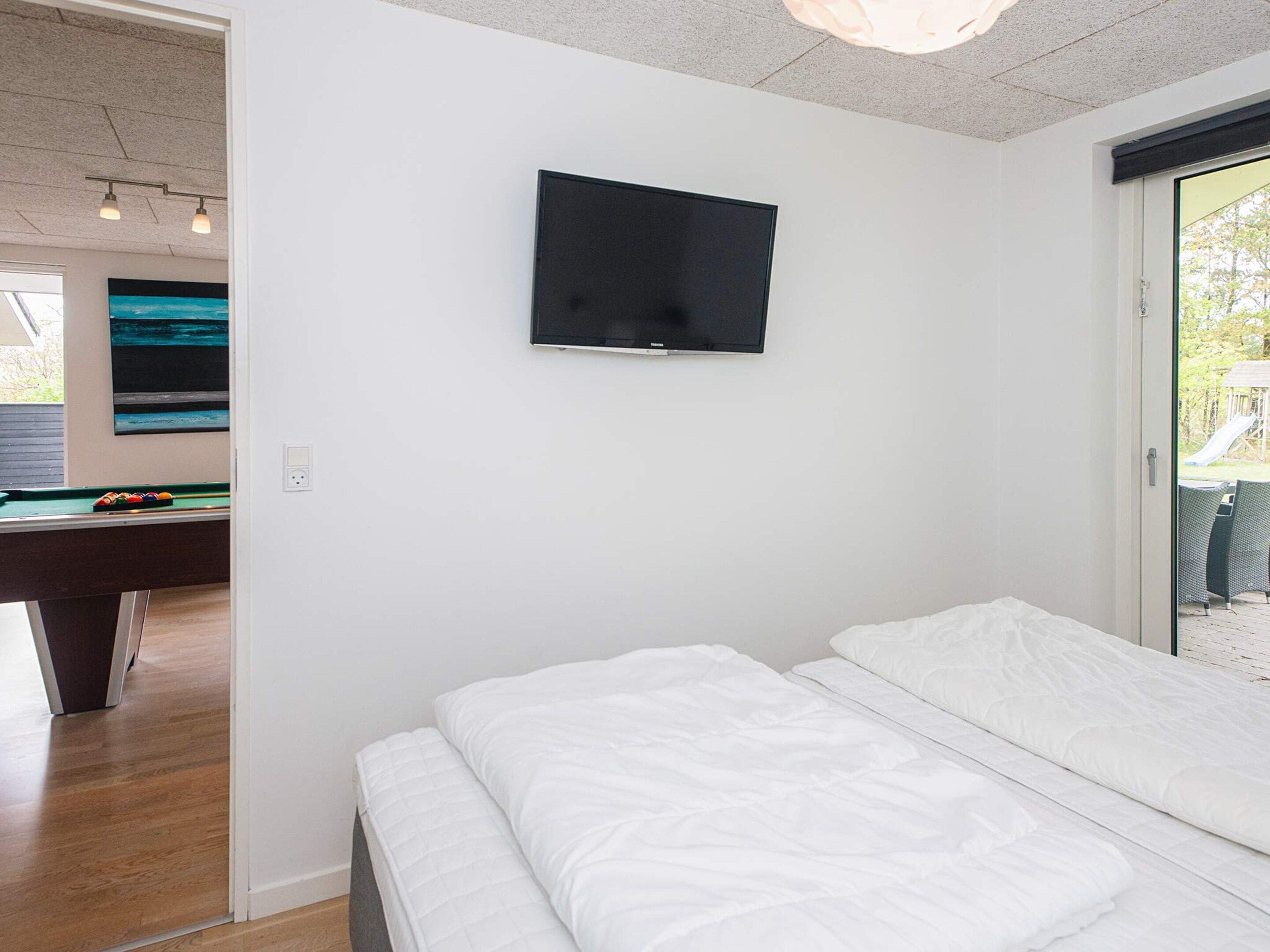 Une chambre à coucher avec un lit, un téléviseur fixé au mur et une table de billard dans la pièce adjacente.